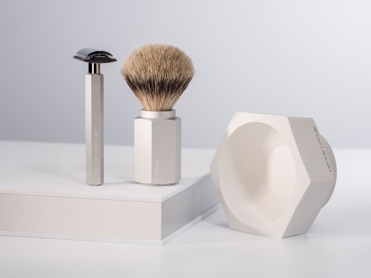 Shaving brush, razor and shaving bowl on a white surface with a light gray background