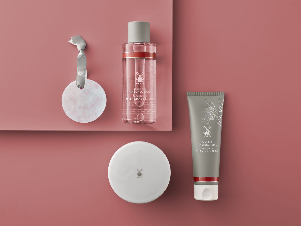 Muhle shaving products, including aftershave lotion, shaving cream, a shaving alum block on a pink background.
