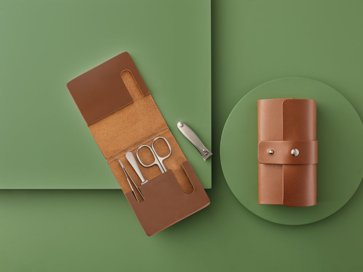A brown leather grooming kit with scissors, tweezers, and nail clippers, displayed on a green background.
