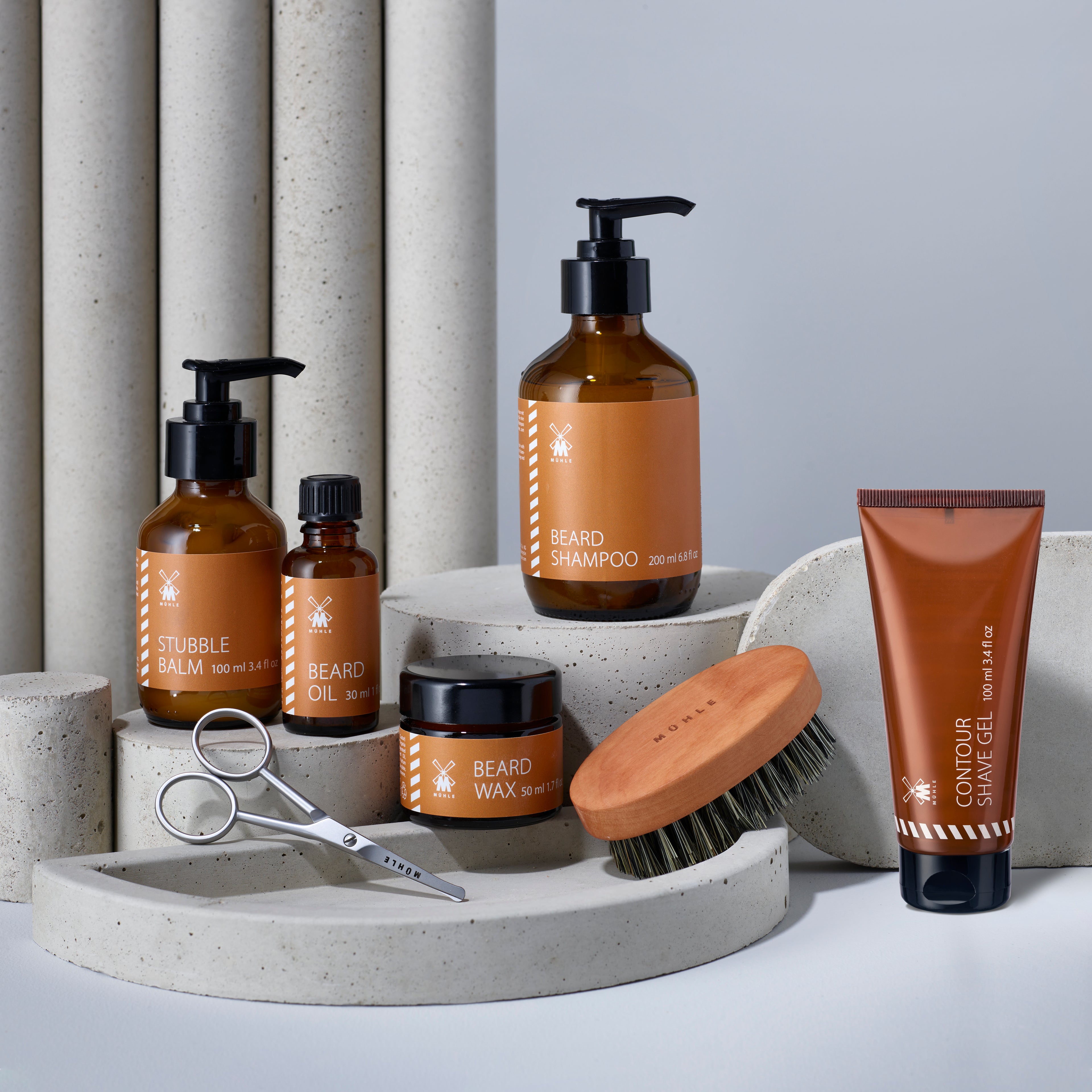 Muhle beard grooming products, including shampoo, balm, oil, wax, contour shave gel, scissors, and a brush on neutral background.
