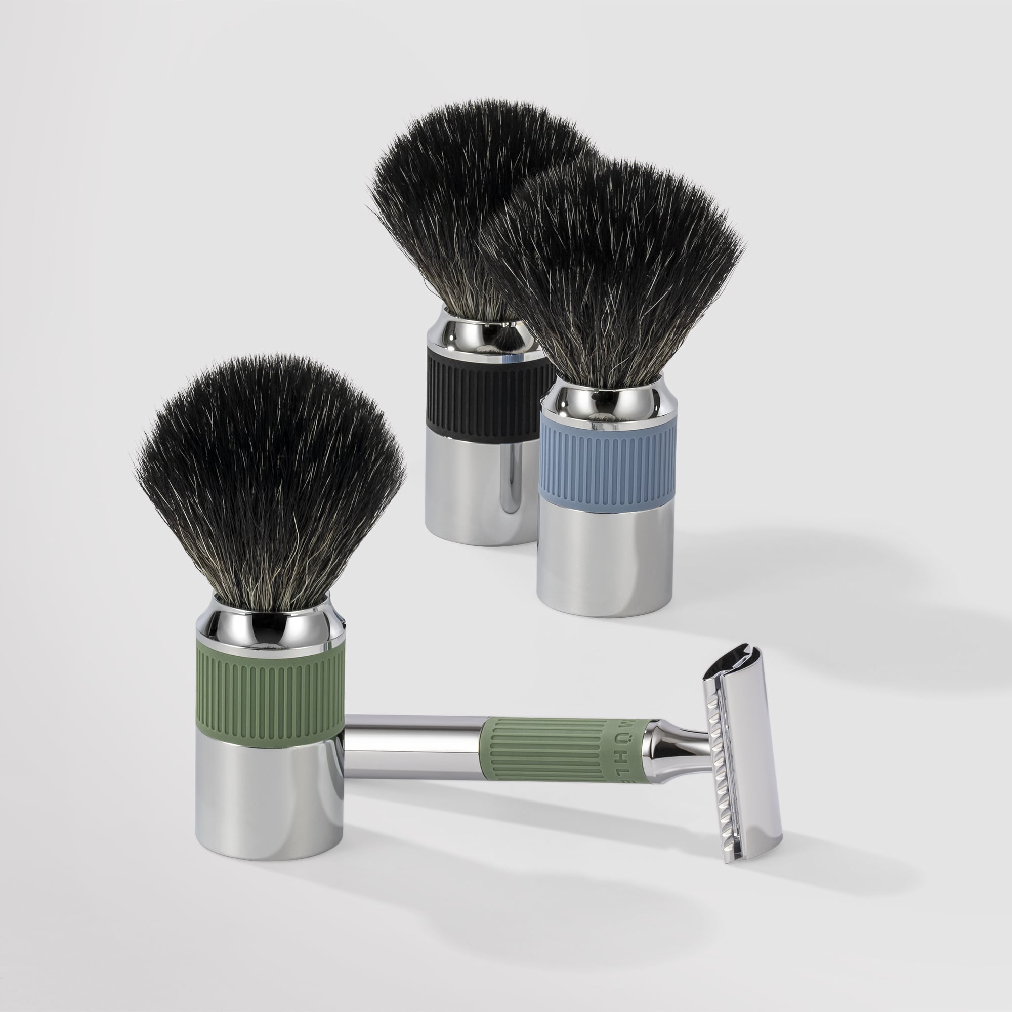 Two Shaving brushes on the background with colored textured handles, one black, the other is light blue and shaving kit of a safety razor and shaving brush with the same green colored textured handle
