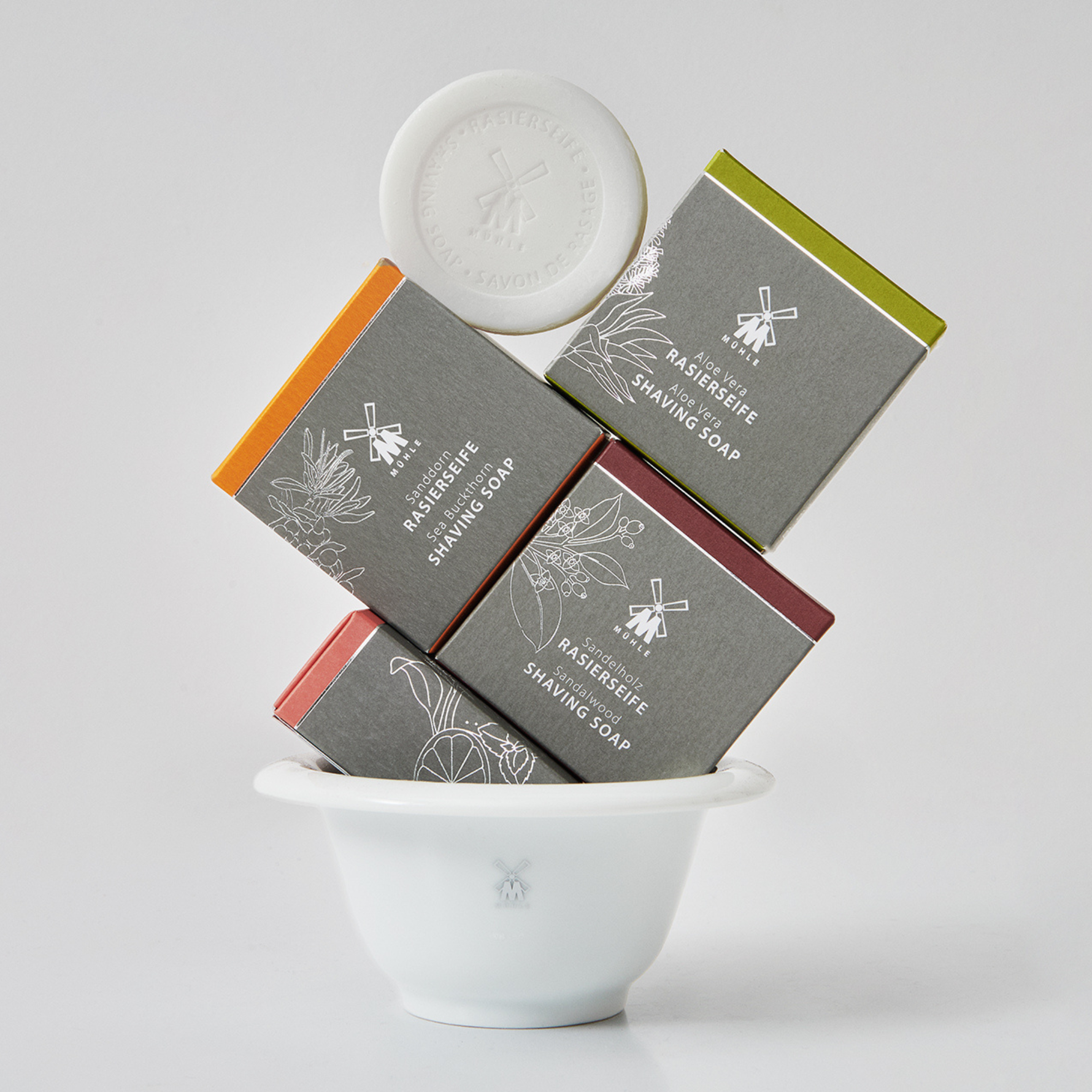 Aloe Vera, Sea Buckthorn, and Sandalwood shaving soap bars with packaging in a white bowl on a light gray background